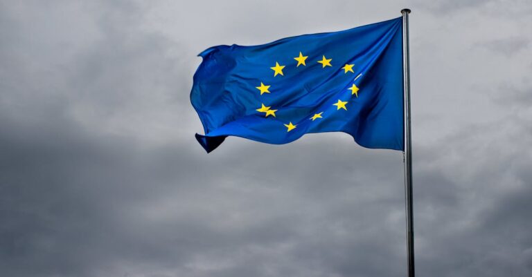 A vibrant EU flag flutters in the breeze against a dramatic cloudy backdrop. Symbol of unity.