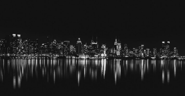 Captivating black and white view of New York City skyline reflecting on water at night.