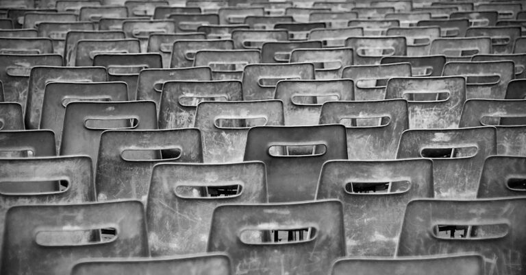 Black-and-white image of empty plastic chairs arranged in rows, creating a pattern.